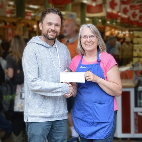 Local Restaurateur and Artist Michael Maxxis accepts donation cheque for $5,000 from Old Strathcona Farmers' Market Board President, Sheila Hamilton. The donation is to fund a community mural by famous Spanish artist, Okuda San Miguel.